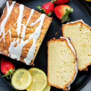 Lemon pound cake with strawberries and icing on a black plate.