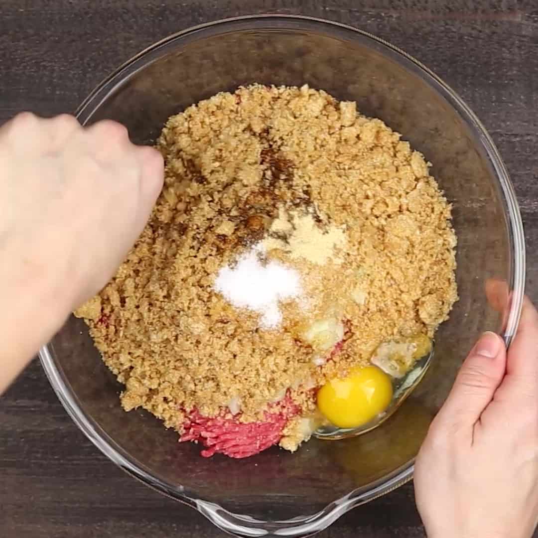 A person mixing keto meatloaf ingredients in a bowl.