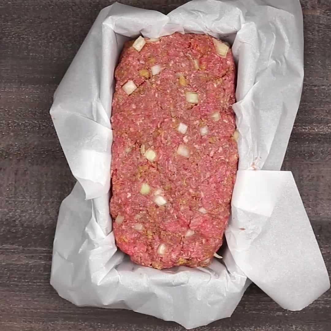 keto meatloaf in parchment paper lined loaf pan on a wooden table.