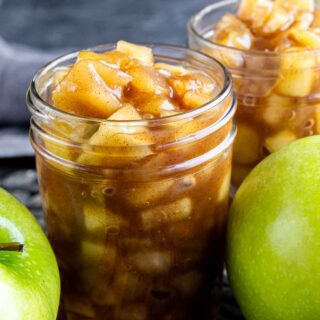 Two jars of apple pie filling on a table.