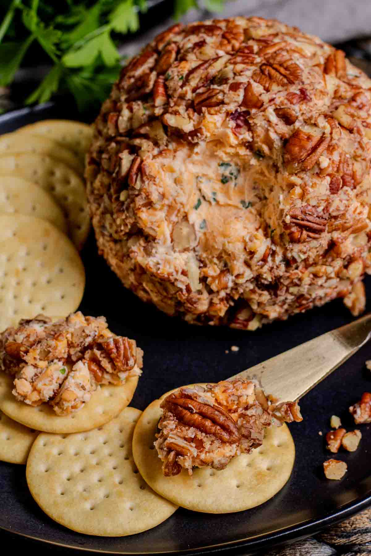 A cheese ball with pecans and crackers on a plate.