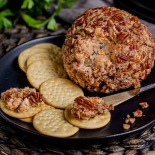 A cheese ball with crackers and pecans on a black plate.