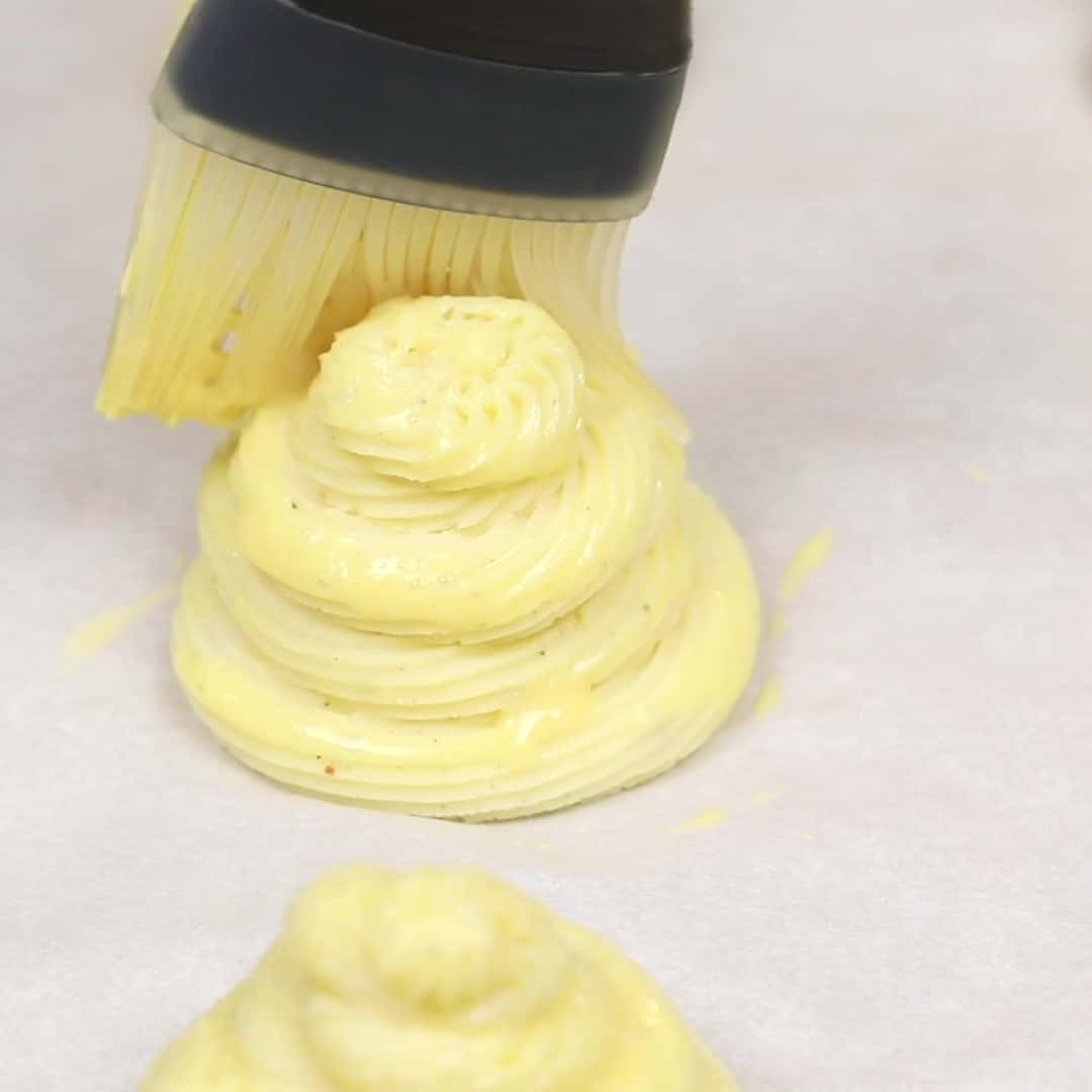 A person is using a brush to egg wash Duchess Potatoes