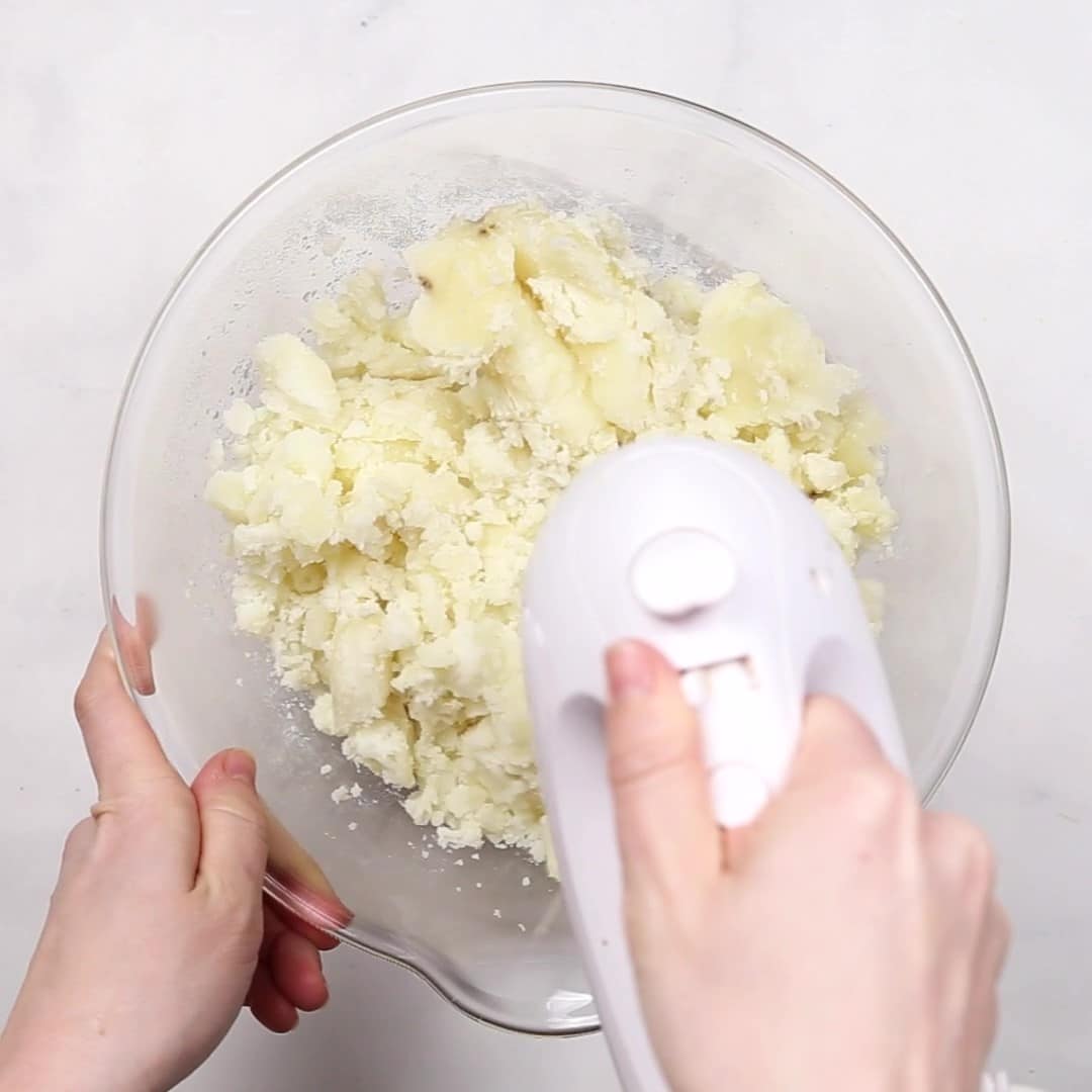 A person using a hand mixer to mash potatoes in a bowl for Duchess Potatoes