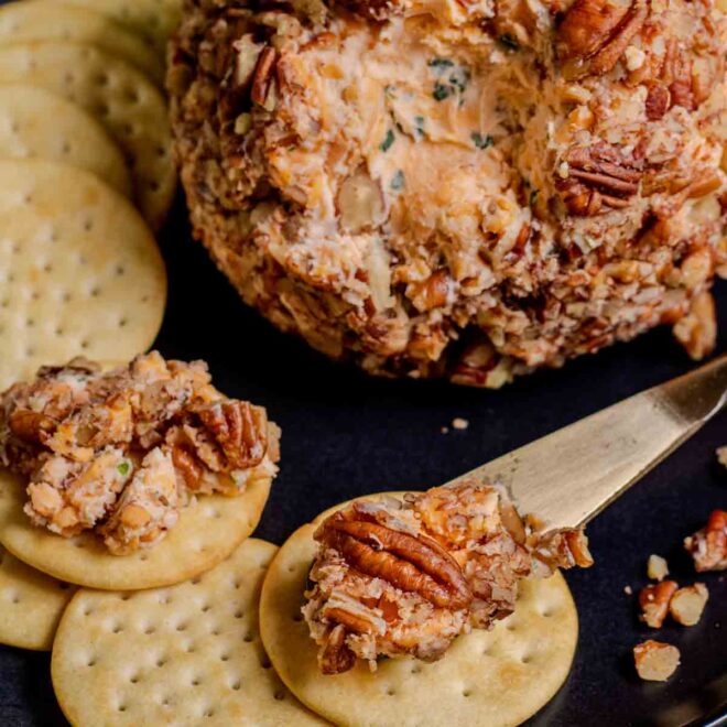 A cheese ball with pecans and crackers on a plate.