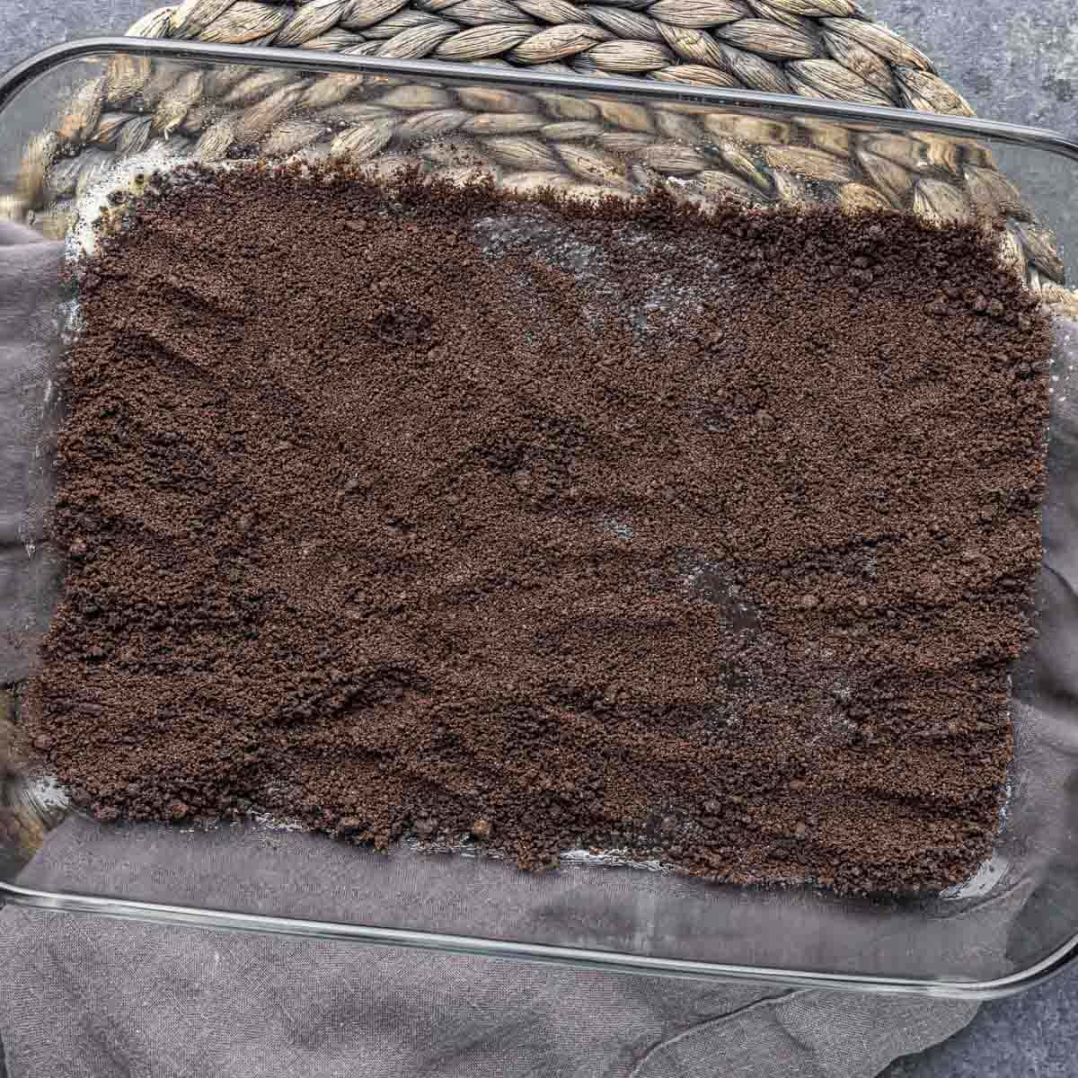 A baking dish filled with a mixture of crushed Oreo to make Oreo Magic Bars.