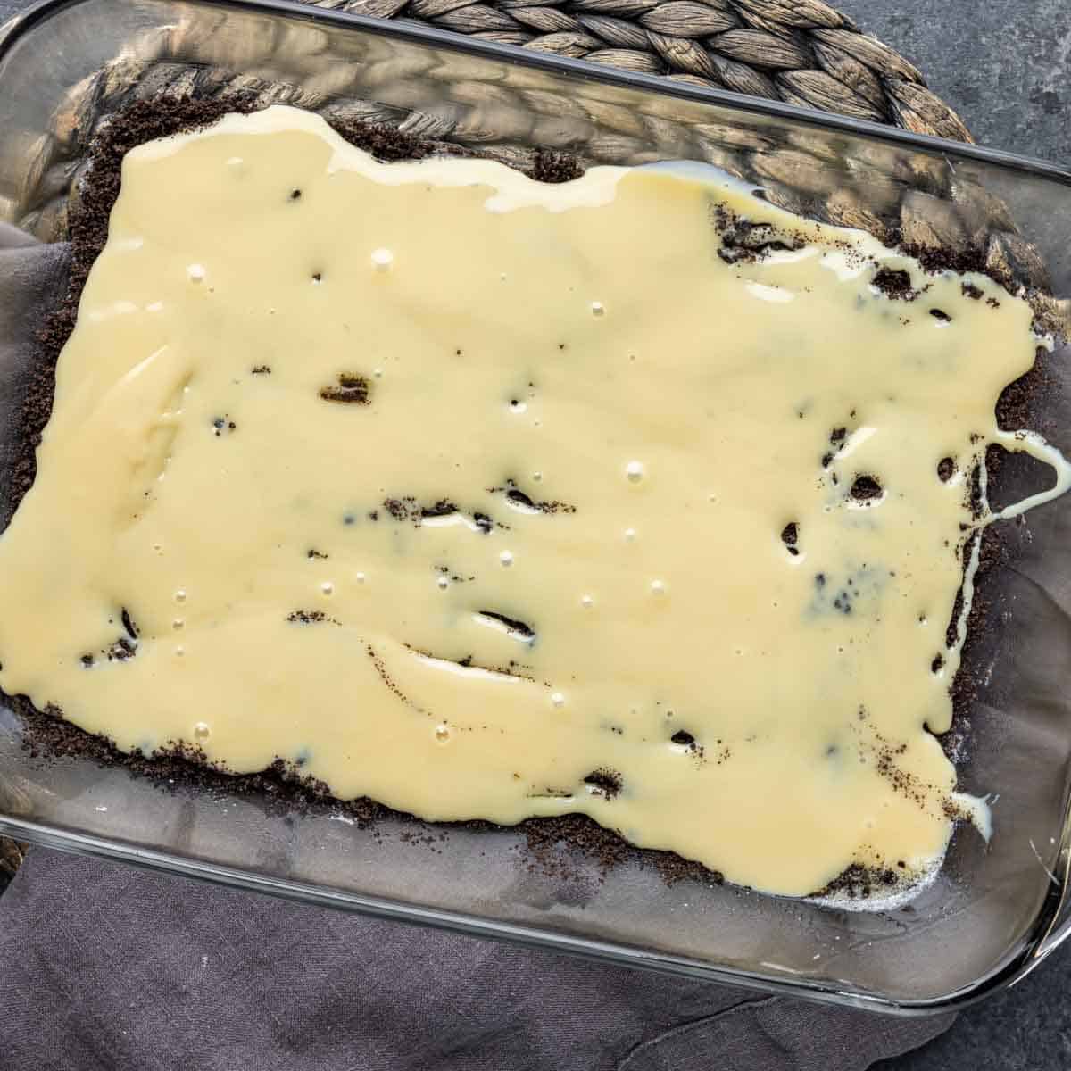 A glass baking dish with a condensed milk layer for Oreo Magic Bars