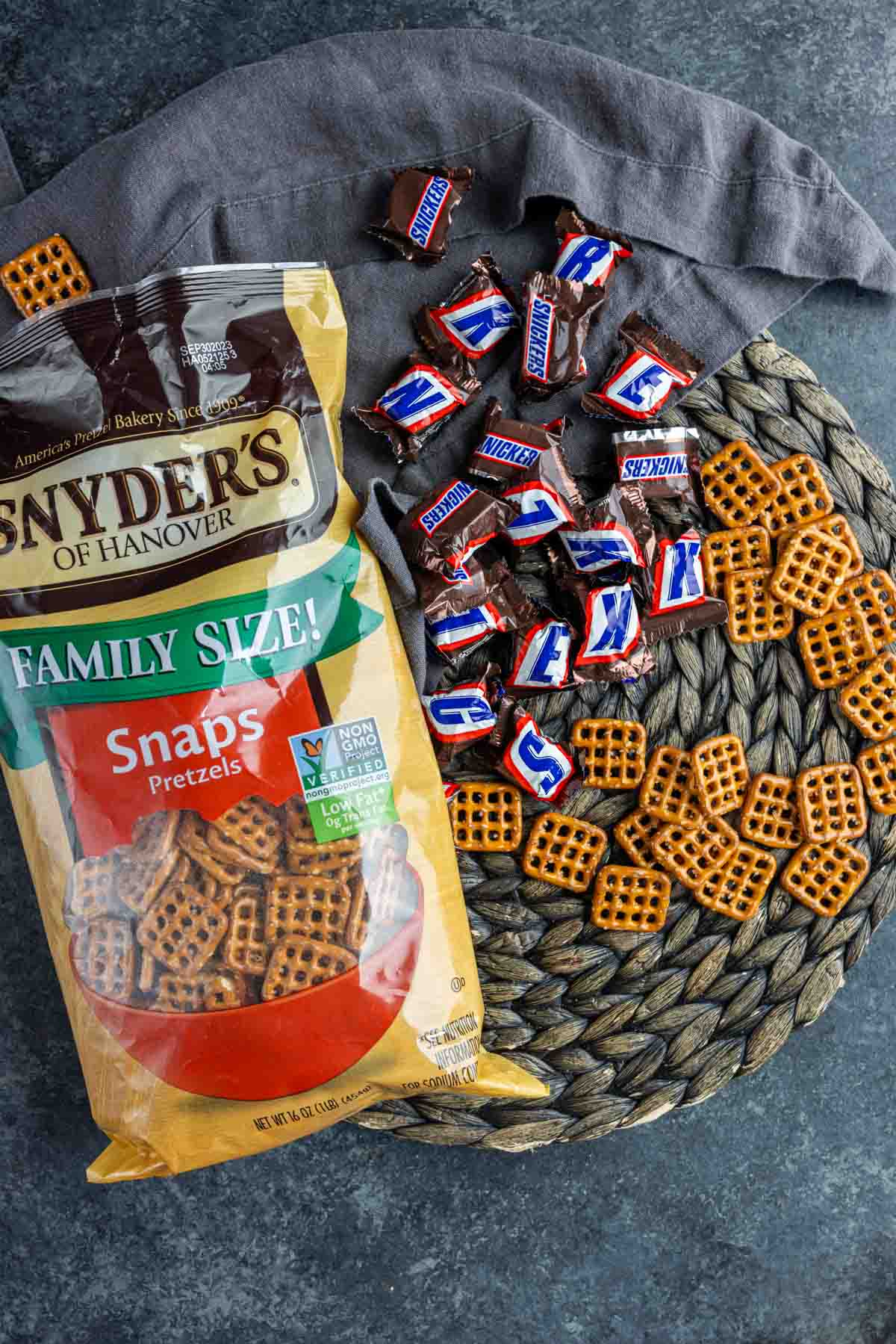 A bag of snyder's family snap pretzels next to Snicker bite size pieces to make Snickers Pretzel Bites