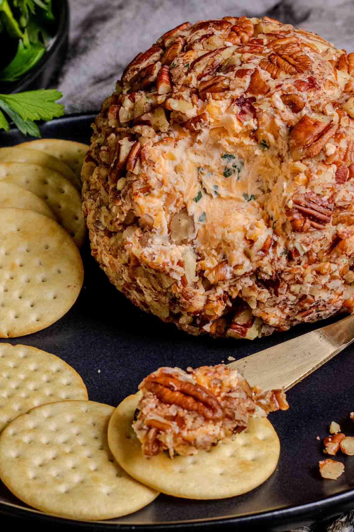 A cheese ball with crackers and nuts on a plate.