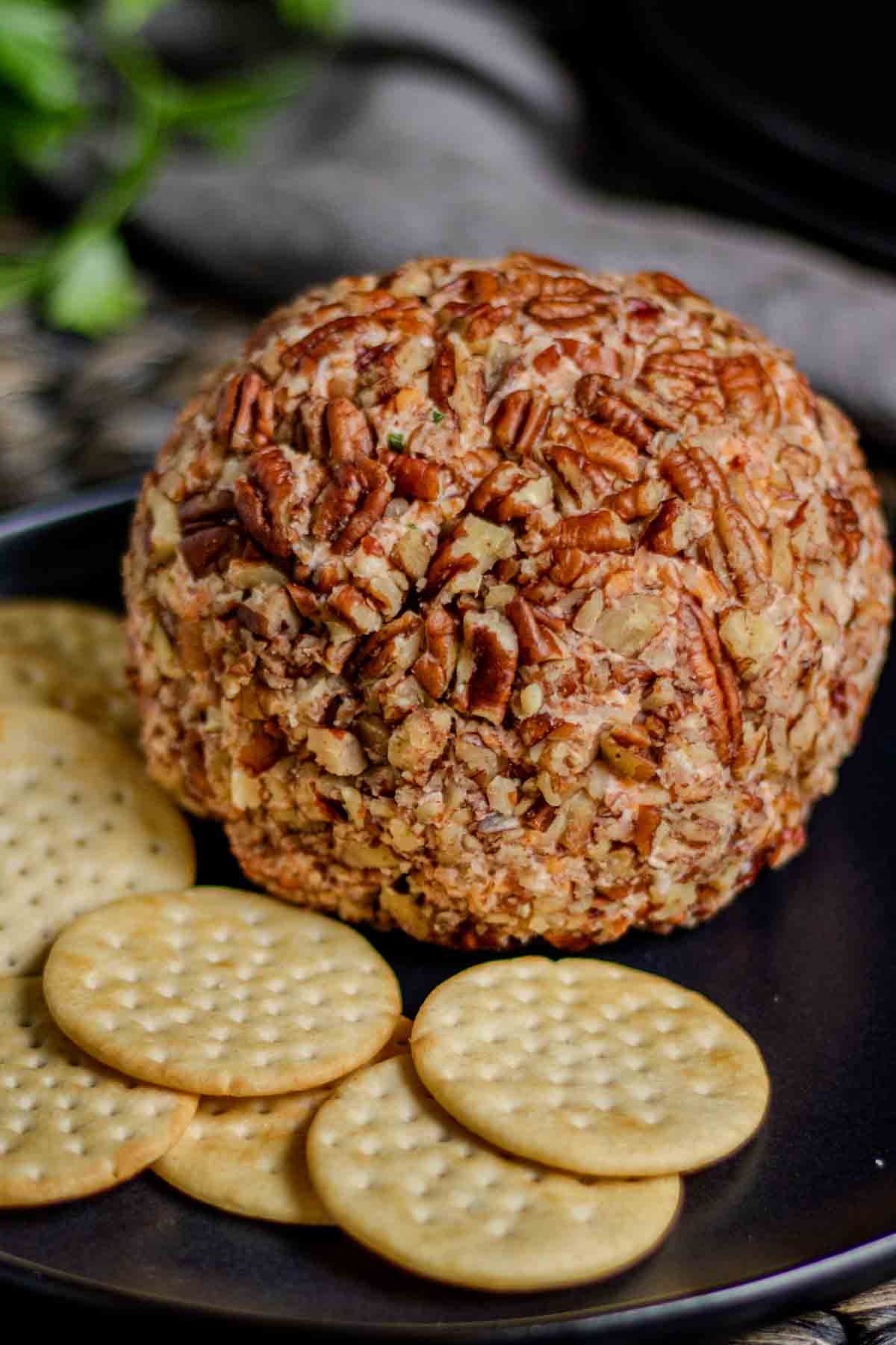 Pecan cheese ball on a black plate with crackers.