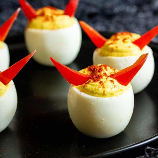 Halloween Deviled Eggs with red horns on a black plate.