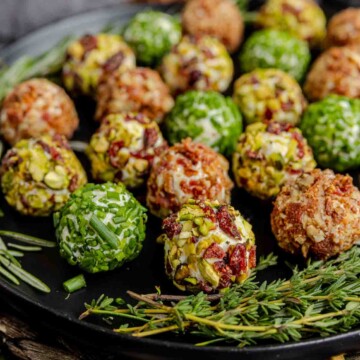 A plate of Mini Cheeseballs 3 Ways on a black plate with sprigs of rosemary.