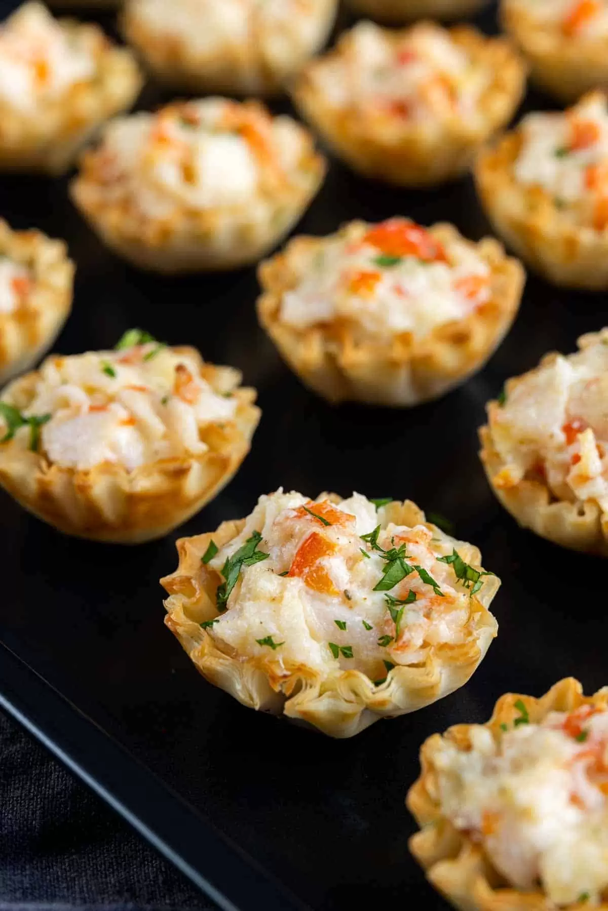 A tray of mini crab puffs with cheese and parsley.