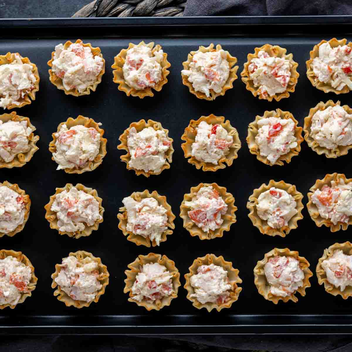 A tray of crab tarts on a black plate.