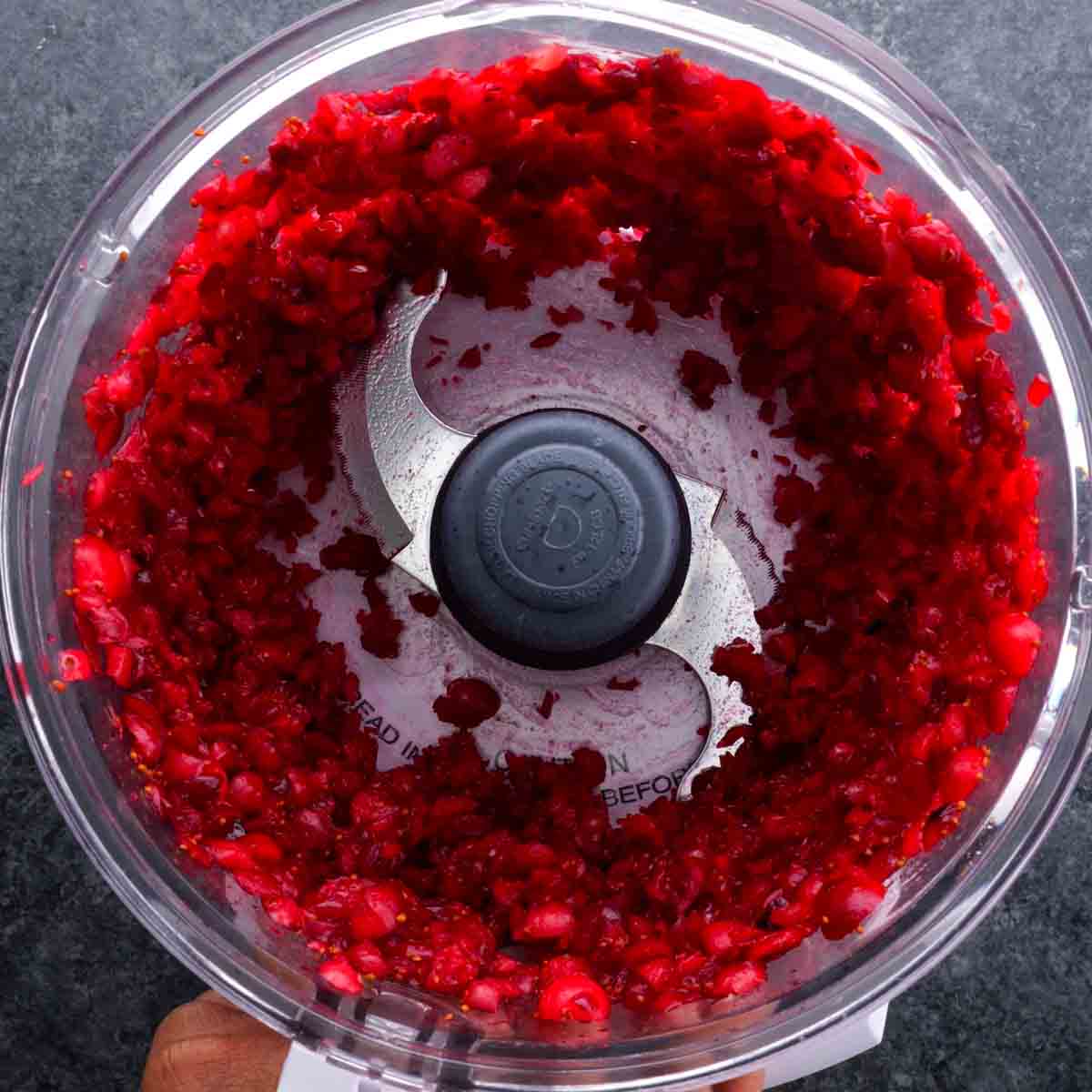A food processor filled with red cranberries to make Cranberry Fluff