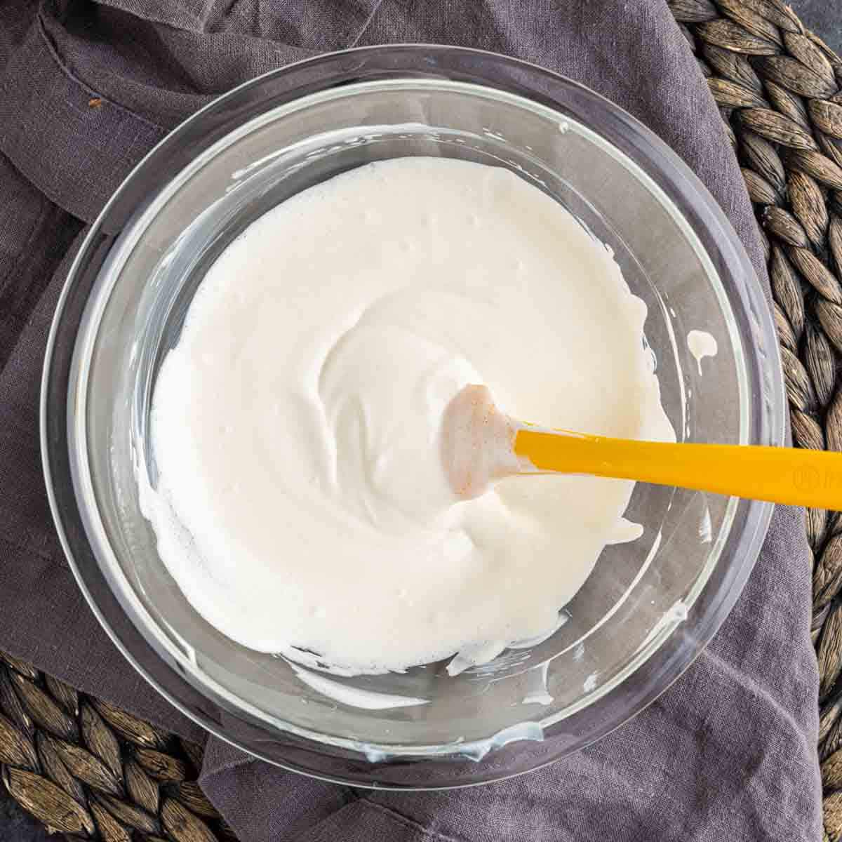 Whipped sour cream in a bowl with a yellow spoon for mini cheesecake topping