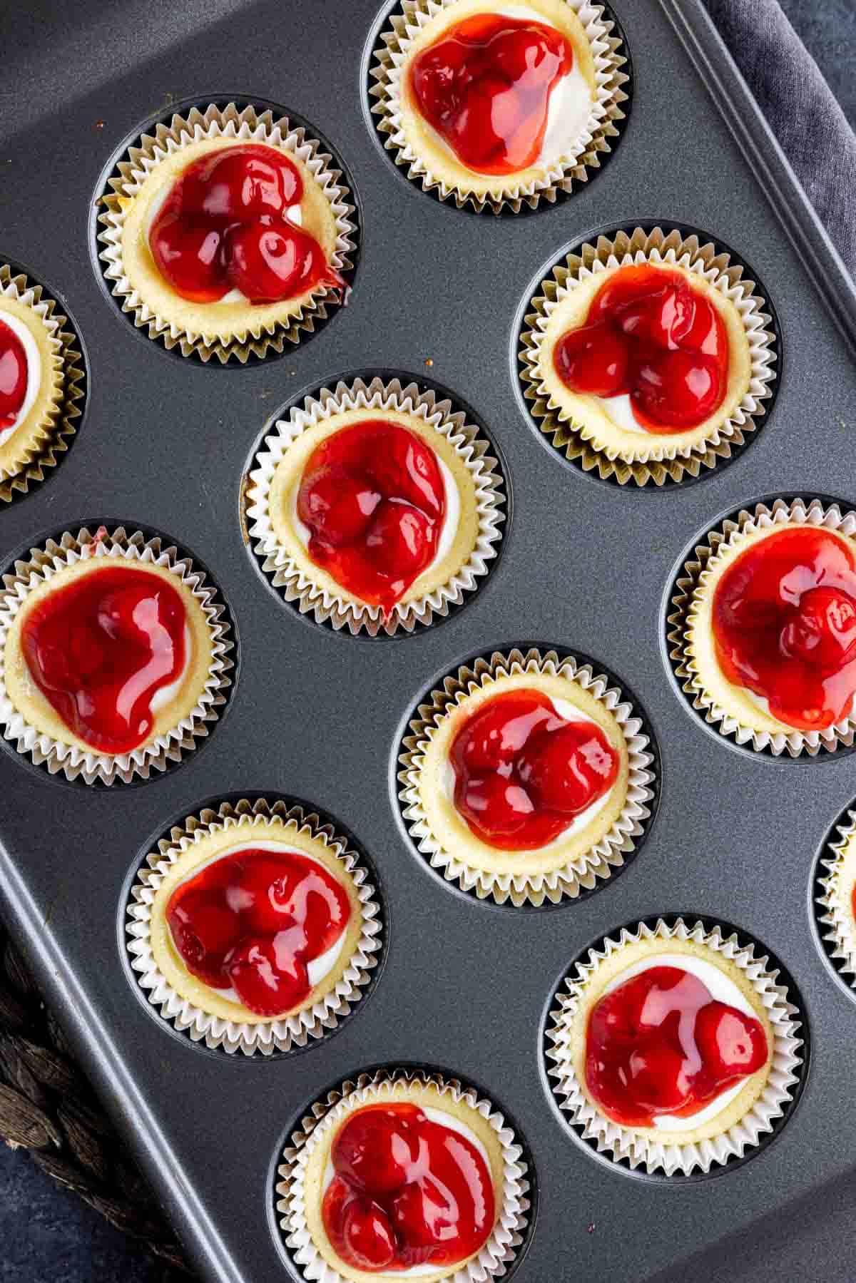 Cherry mini cheesecake cupcakes in a muffin tin.