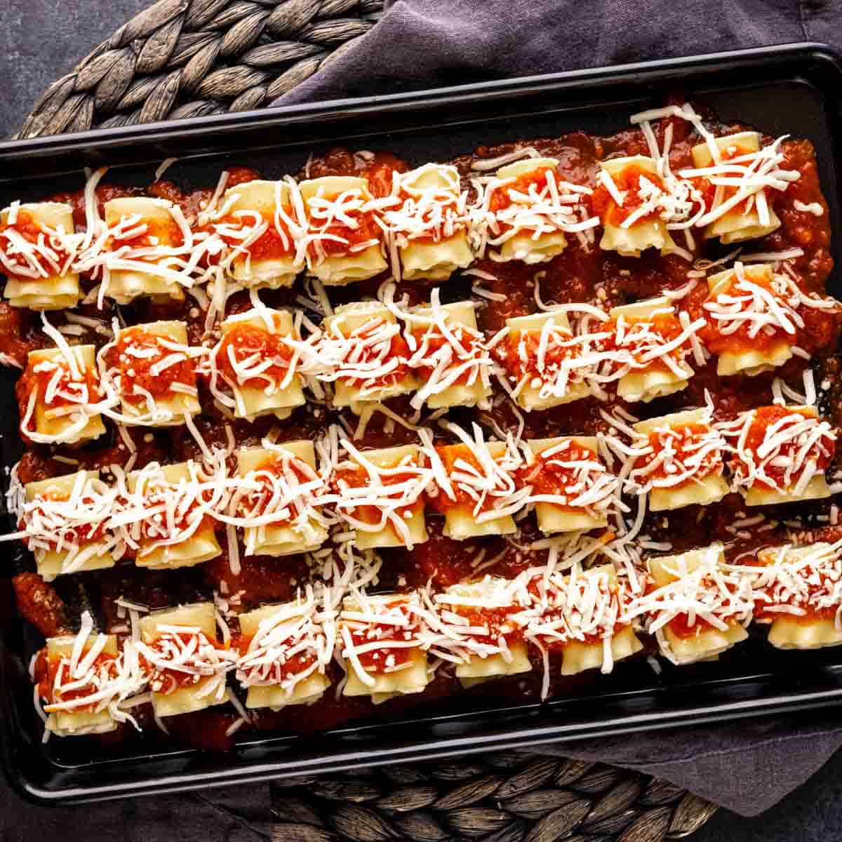 A tray of mini lasagna appetizer filled with sauce and cheese.