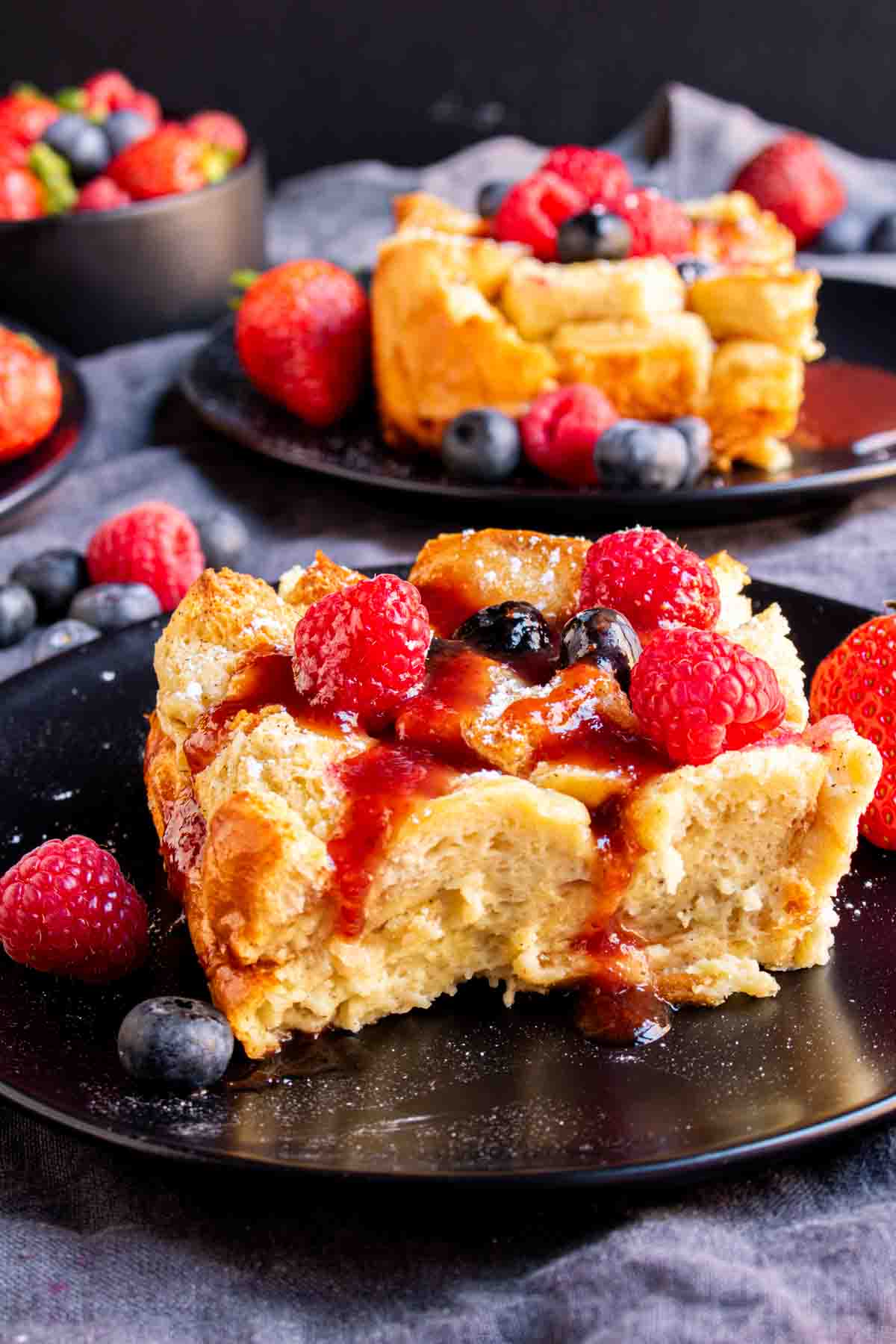 A slice of Overnight French Toast Bake with berries and syrup on a plate.