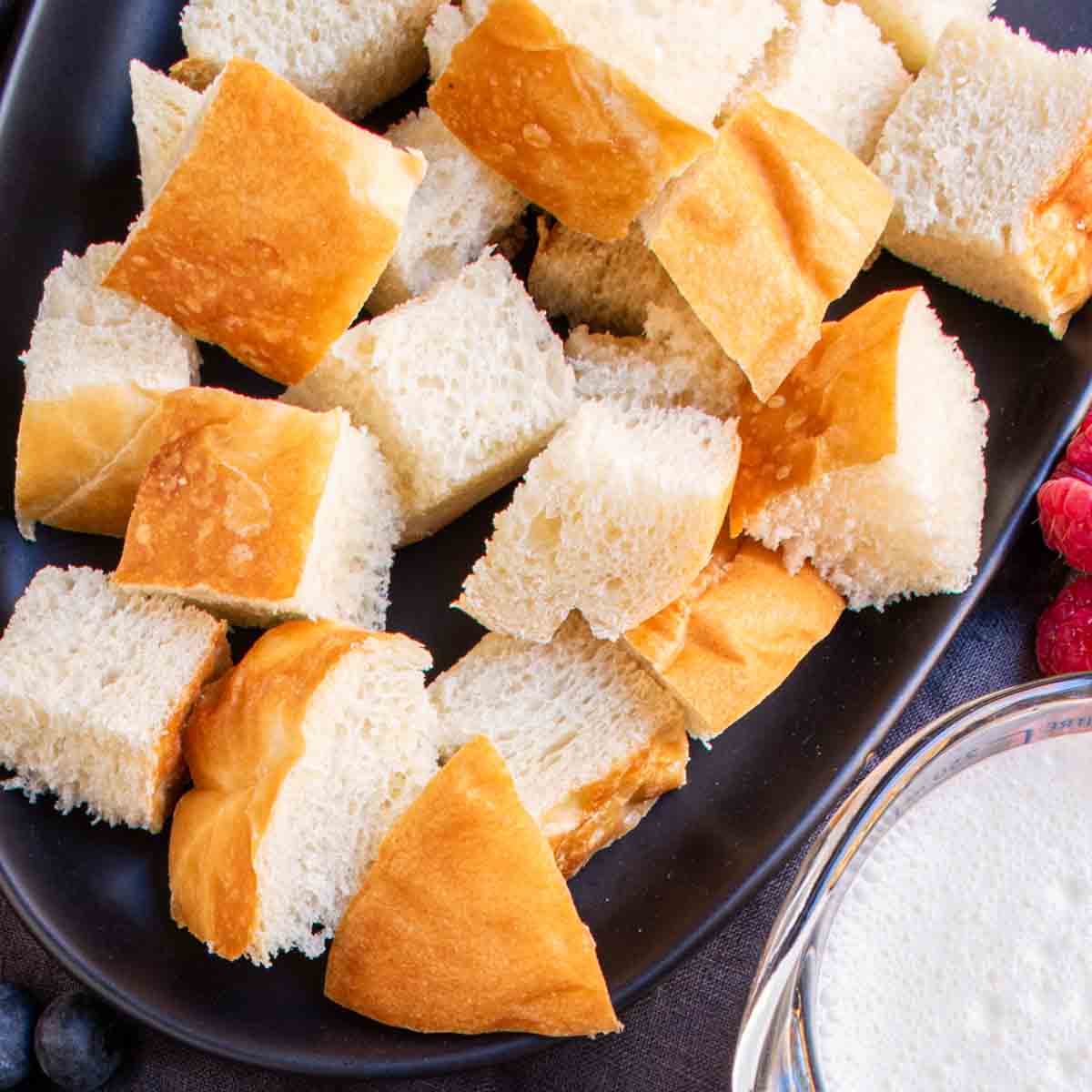 Bread cubes on a black plate with berries and milk for Overnight French Toast Bake