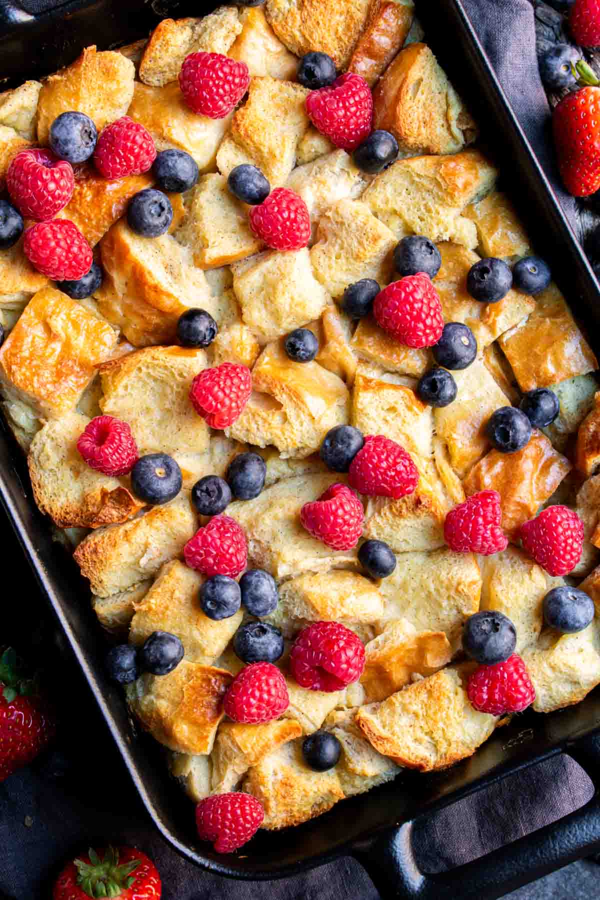 Overnight French Toast Bake with berries and blueberries in a black pan.