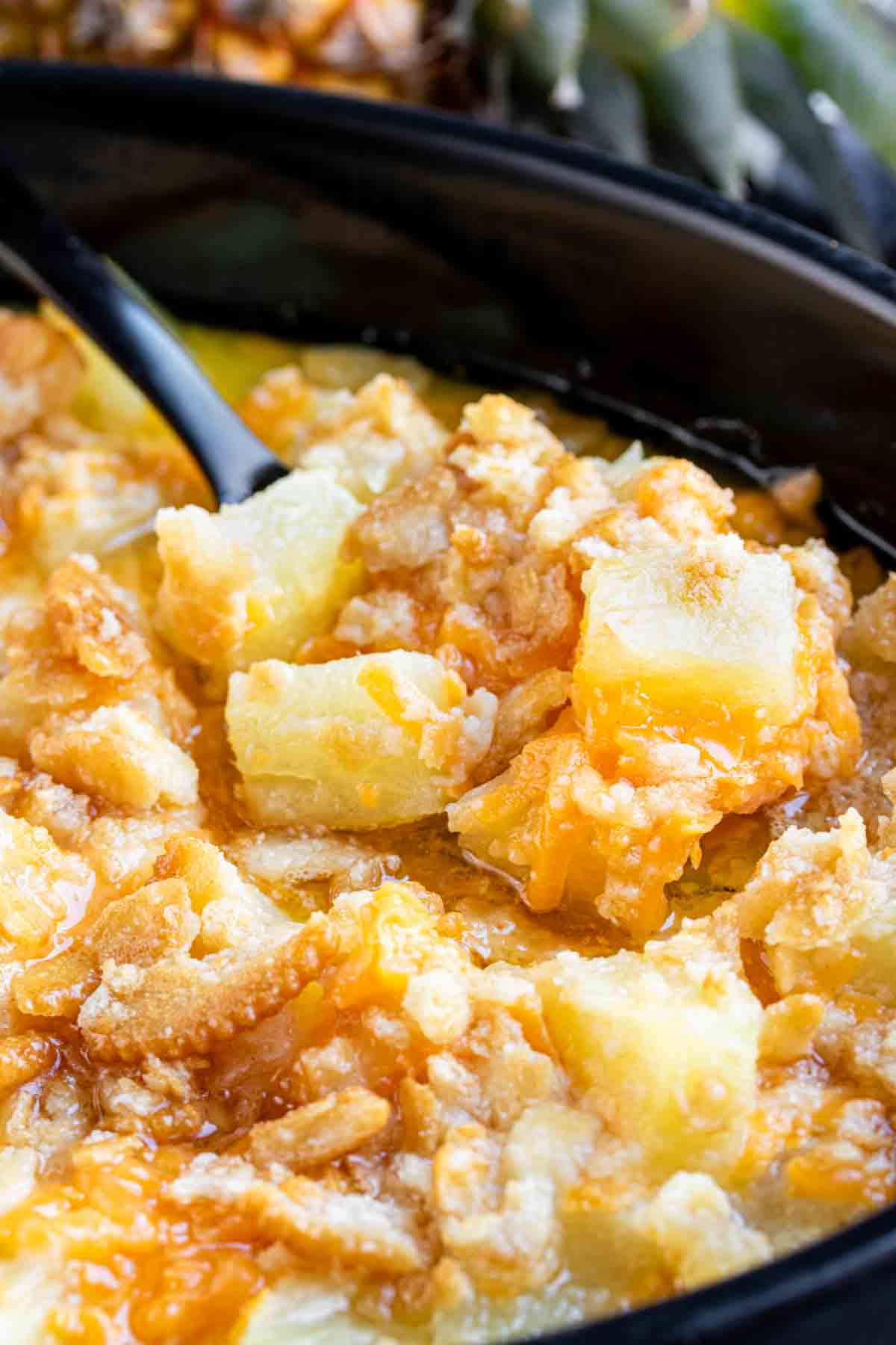 A bowl of cheesy pineapple casserole with a spoon.