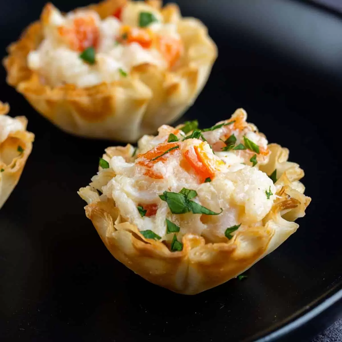 Crab puff pastry cups with crabmeat and parsley on a black plate.