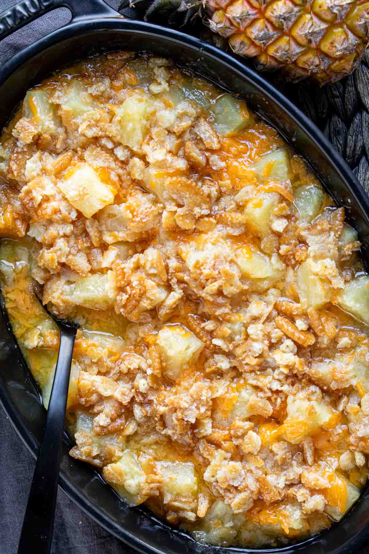 Pineapple casserole in a black skillet with a spoon.