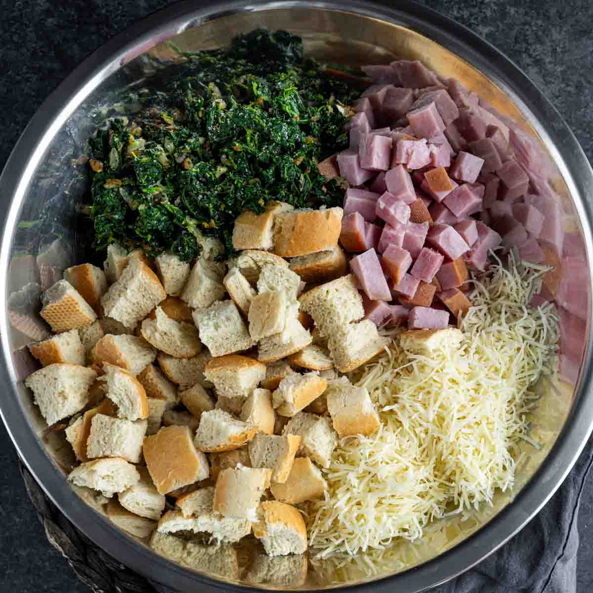 A bowl with ham, cheese, spinach and cubed bread for Ham and Cheese Strata.
