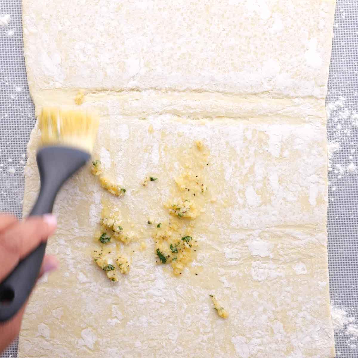 A person using a brush to brush butter on a piece of dough.