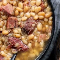 Ham and beans in a black bowl with a spoon.