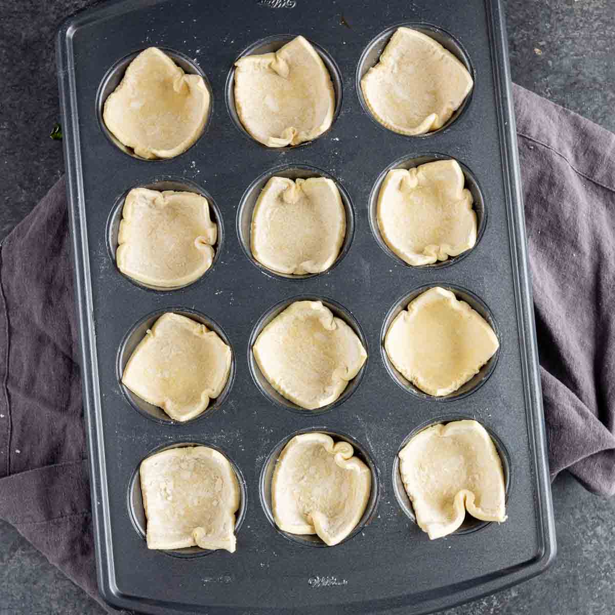 A muffin tin filled with dough for Spinach Puffs