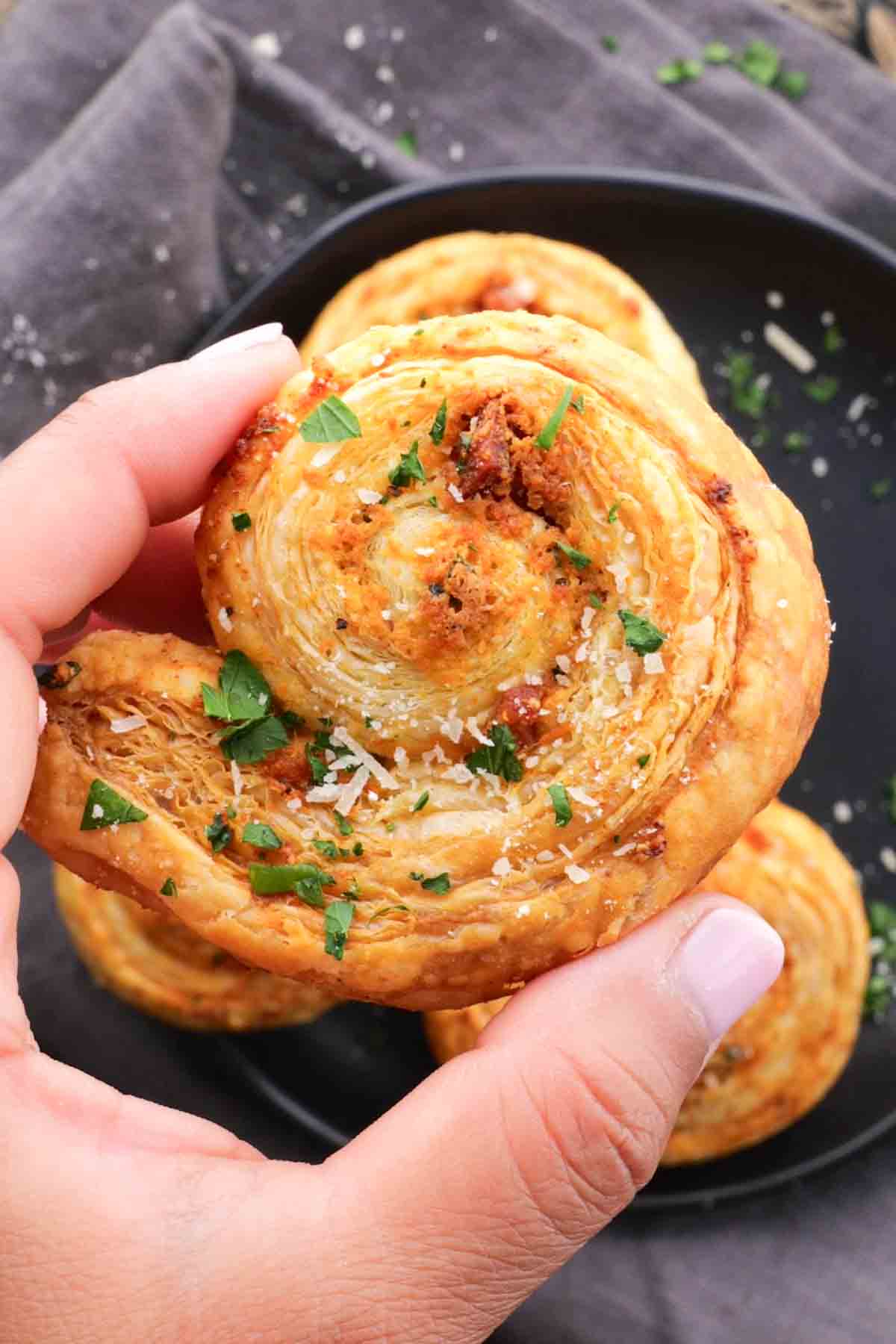 A hand holding a pastry with parmesan cheese and parsley.