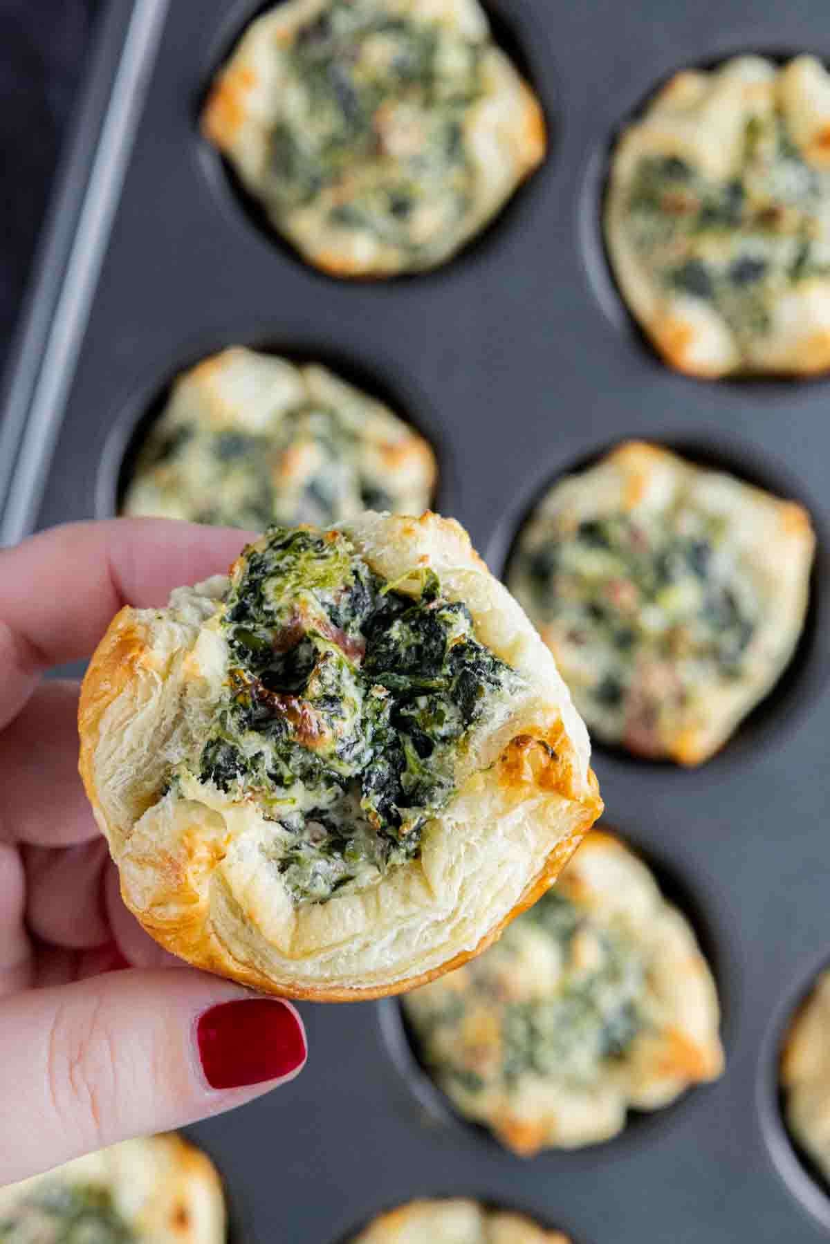 A hand holding up a Spinach Puffs in a muffin tin.