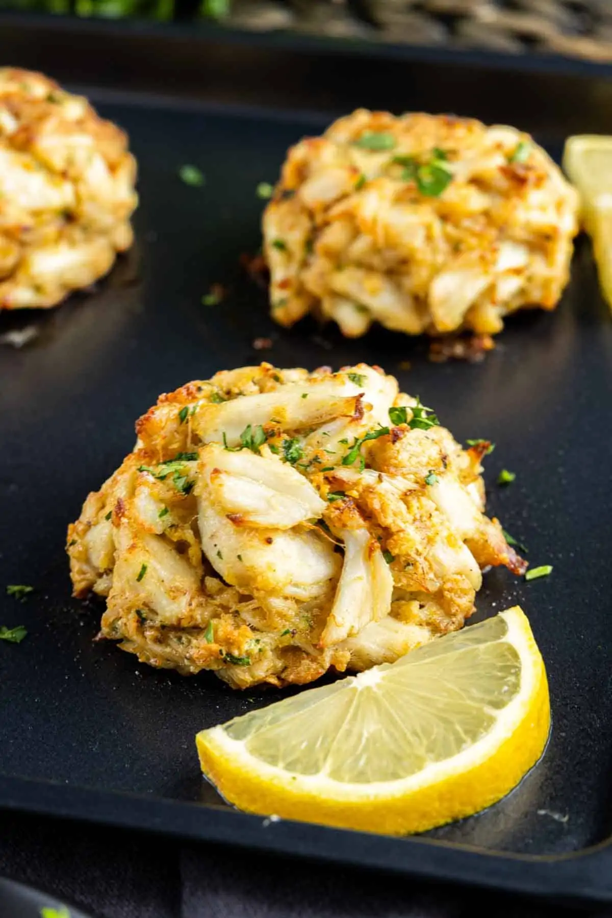 Maryland Crab Cakes on a black tray with lemon wedges.