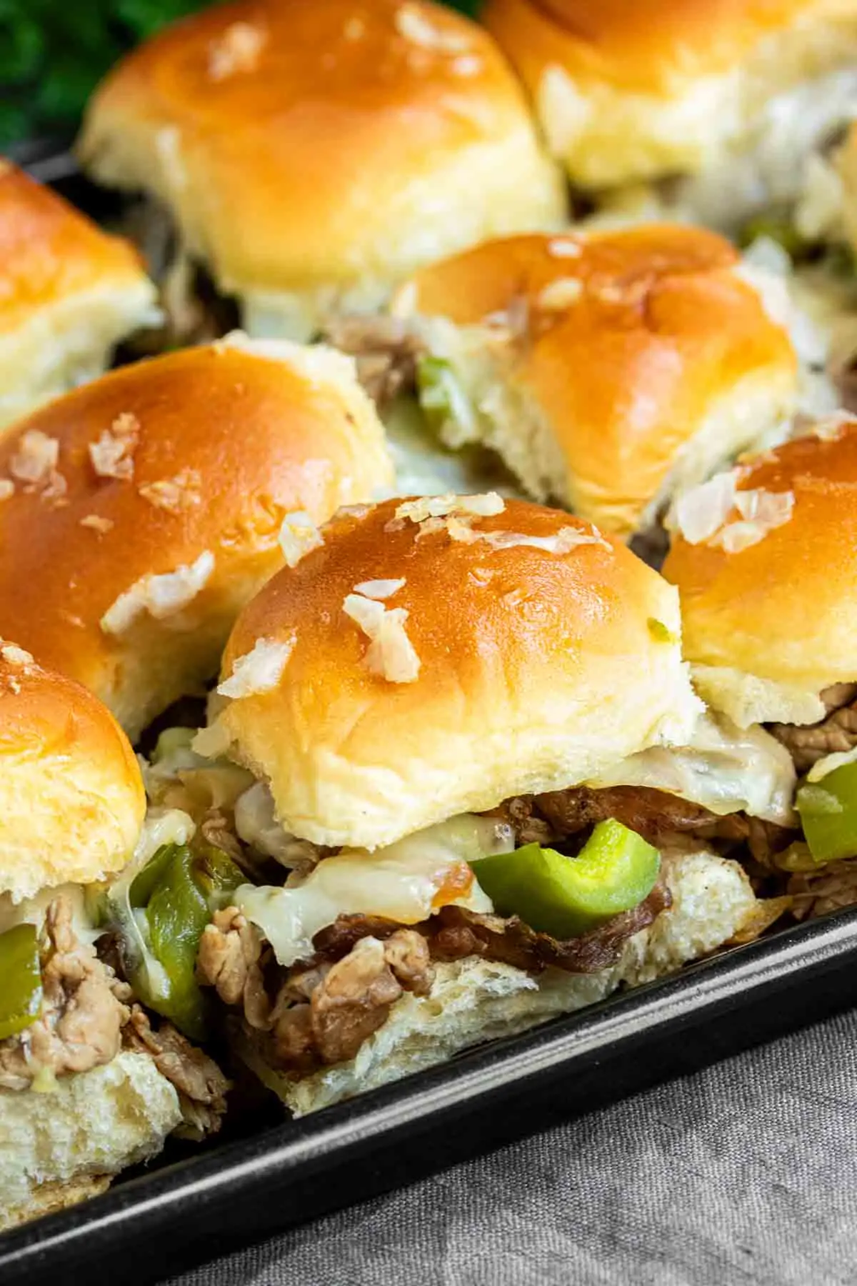 A tray of Philly Cheesesteak Sliders with peppers and onions.