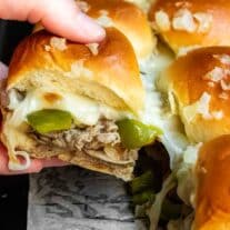 A person is holding philly cheesesteak sliders