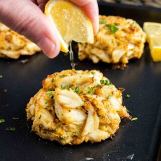 A person drizzling lemon over a batch of Maryland Crab Cakes.