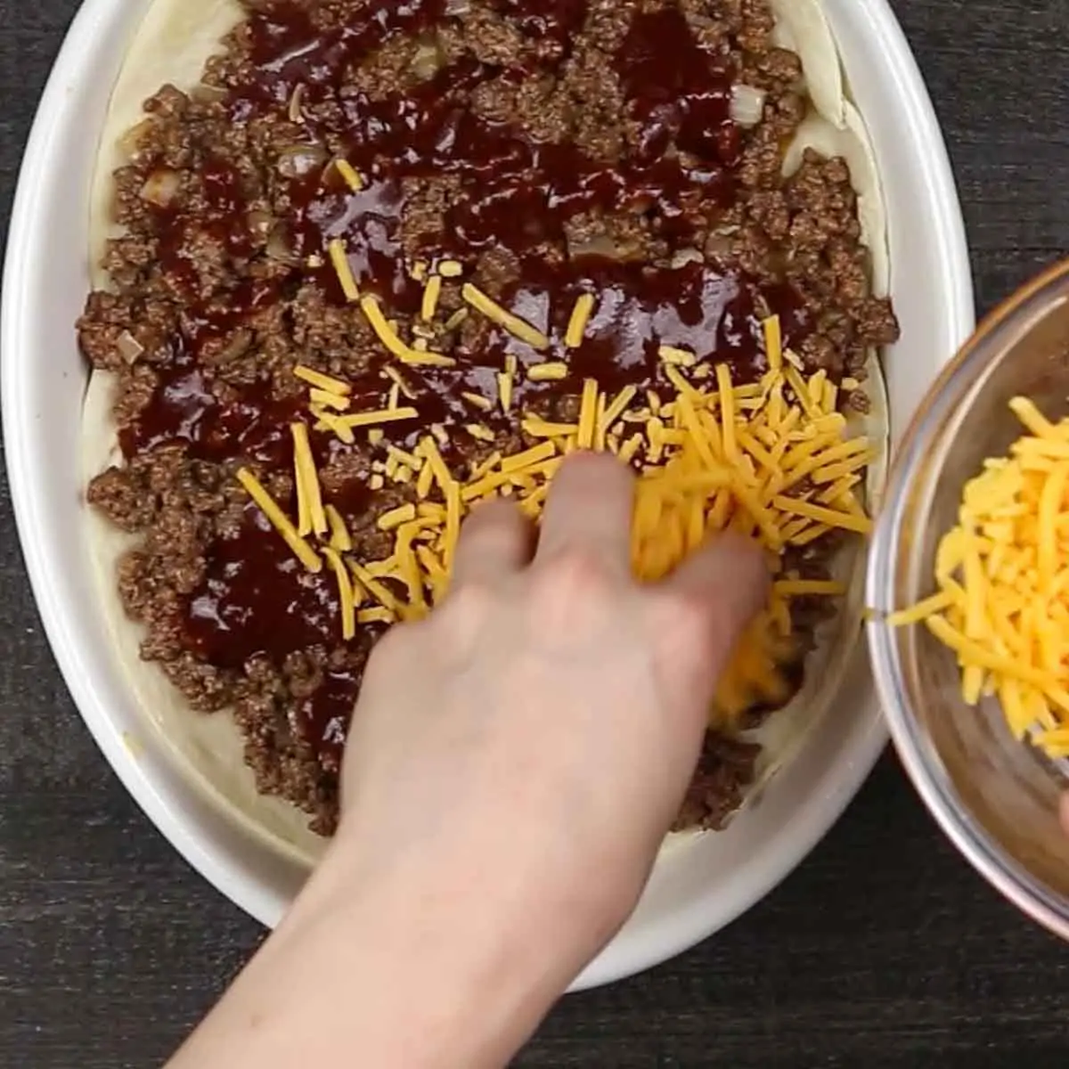 A person putting cheese on top of a Beef Enchilada Casserole