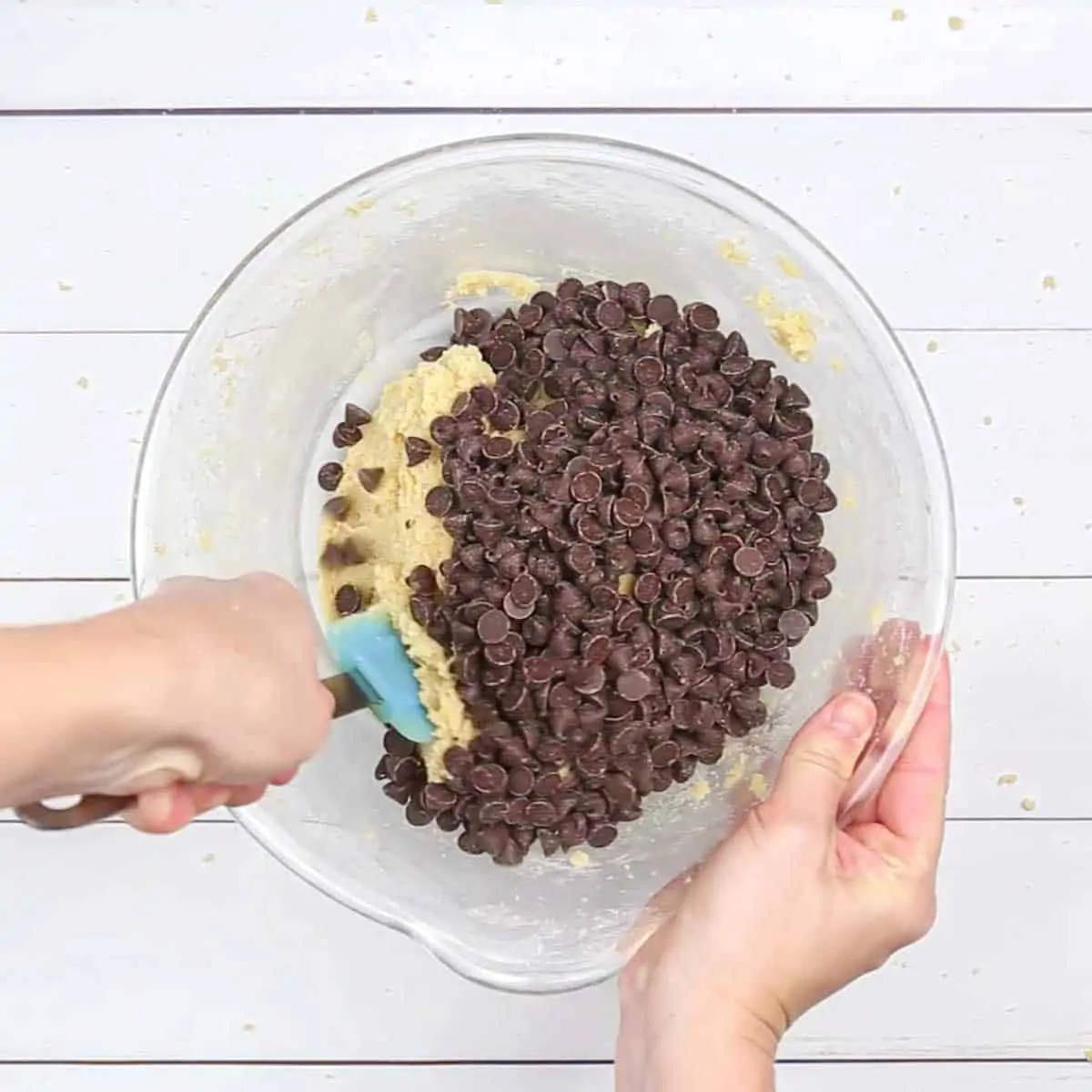 A person scooping chocolate chips into a Brownie Cake dough.