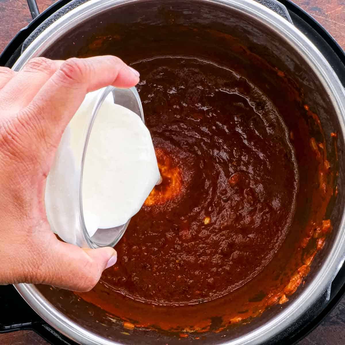 A person pouring cream into an instant pot to make Instant Pot Butter Chicken
