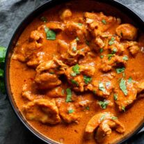 A bowl of Instant Pot Butter Chicken with a sauce and herbs.