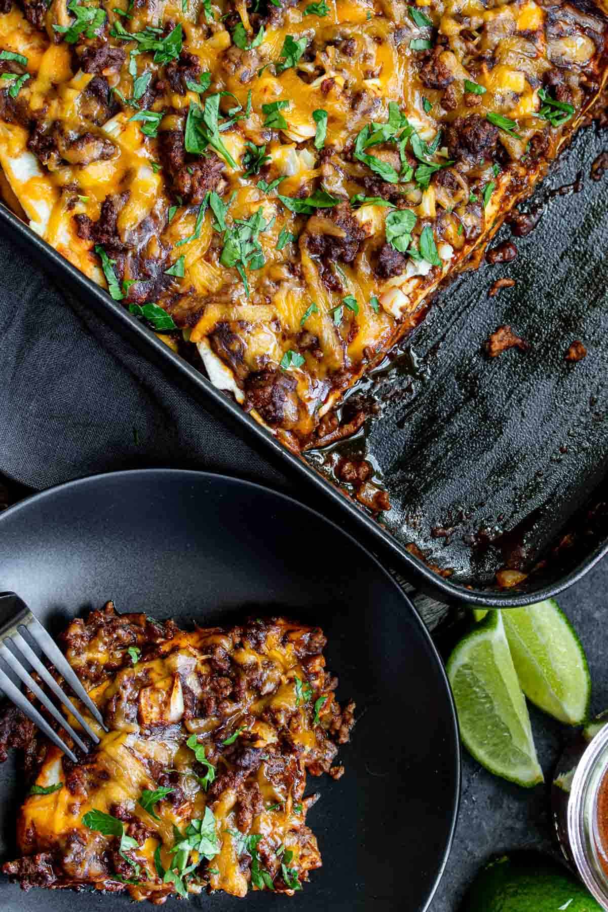 Beef enchilada casserole on a black plate with a fork.