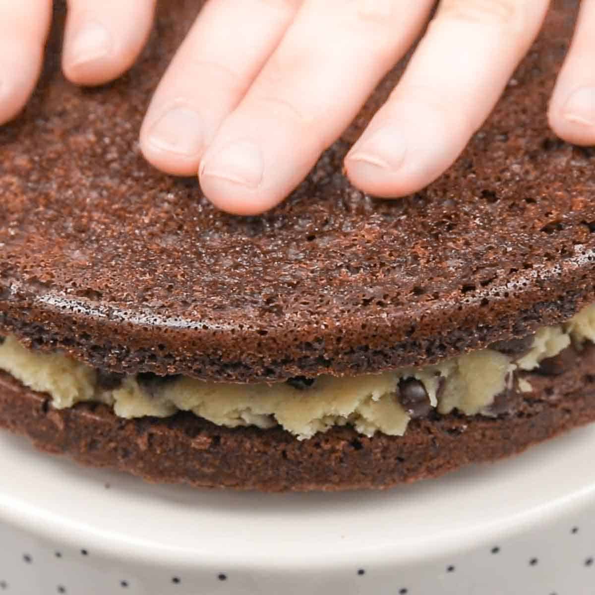 A person's hand on top of a brownie cake