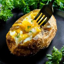 Air Fryer Baked Potato with melted cheese and parsley on a black plate with a fork.