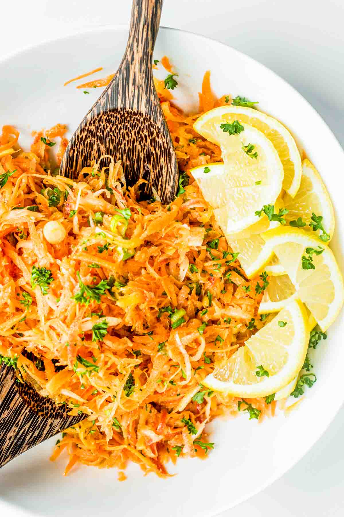 A plate of shredded carrot salad garnished with lemon slices and parsley, served with wooden utensils.