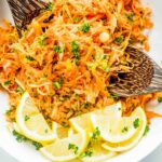 A bowl of shredded carrot salad garnished with lemon slices and parsley.