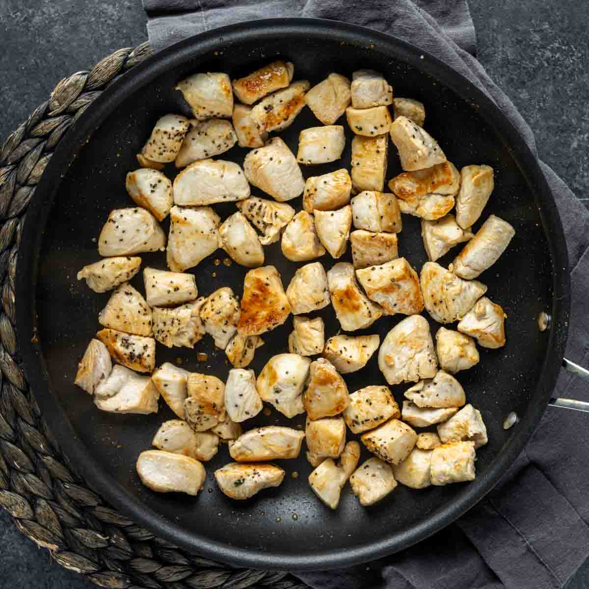 Diced chicken breast pieces being cooked in a frying pan for Chicken Florentine Casserole