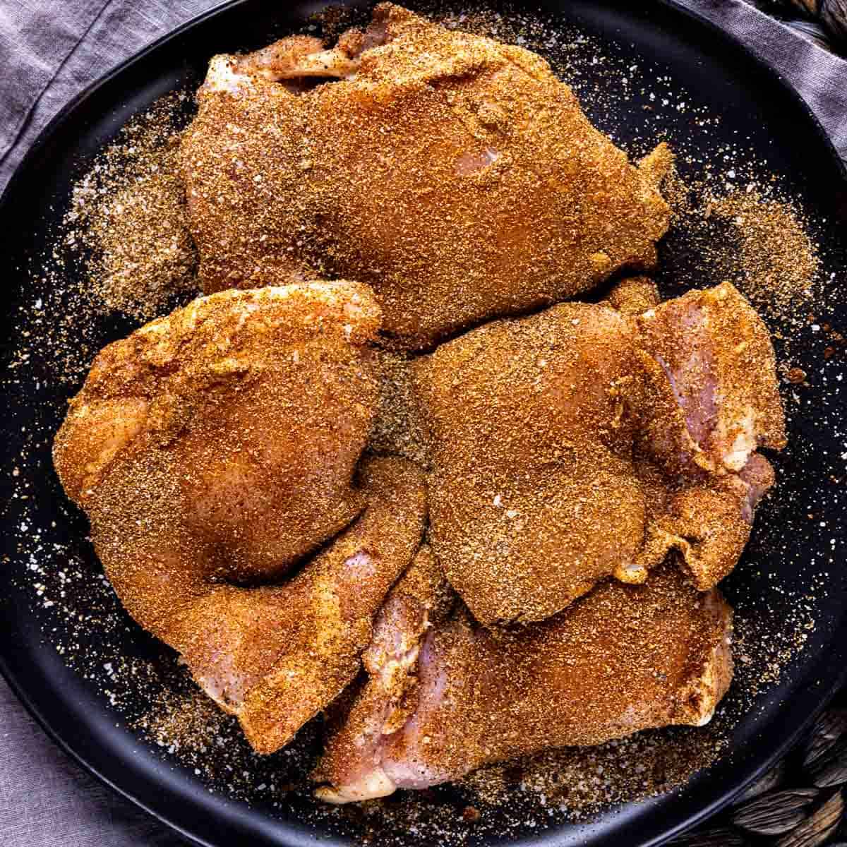 Raw chicken thighs coated with dry rub seasoning on a black plate for One Pot Mexican Chicken and Rice
