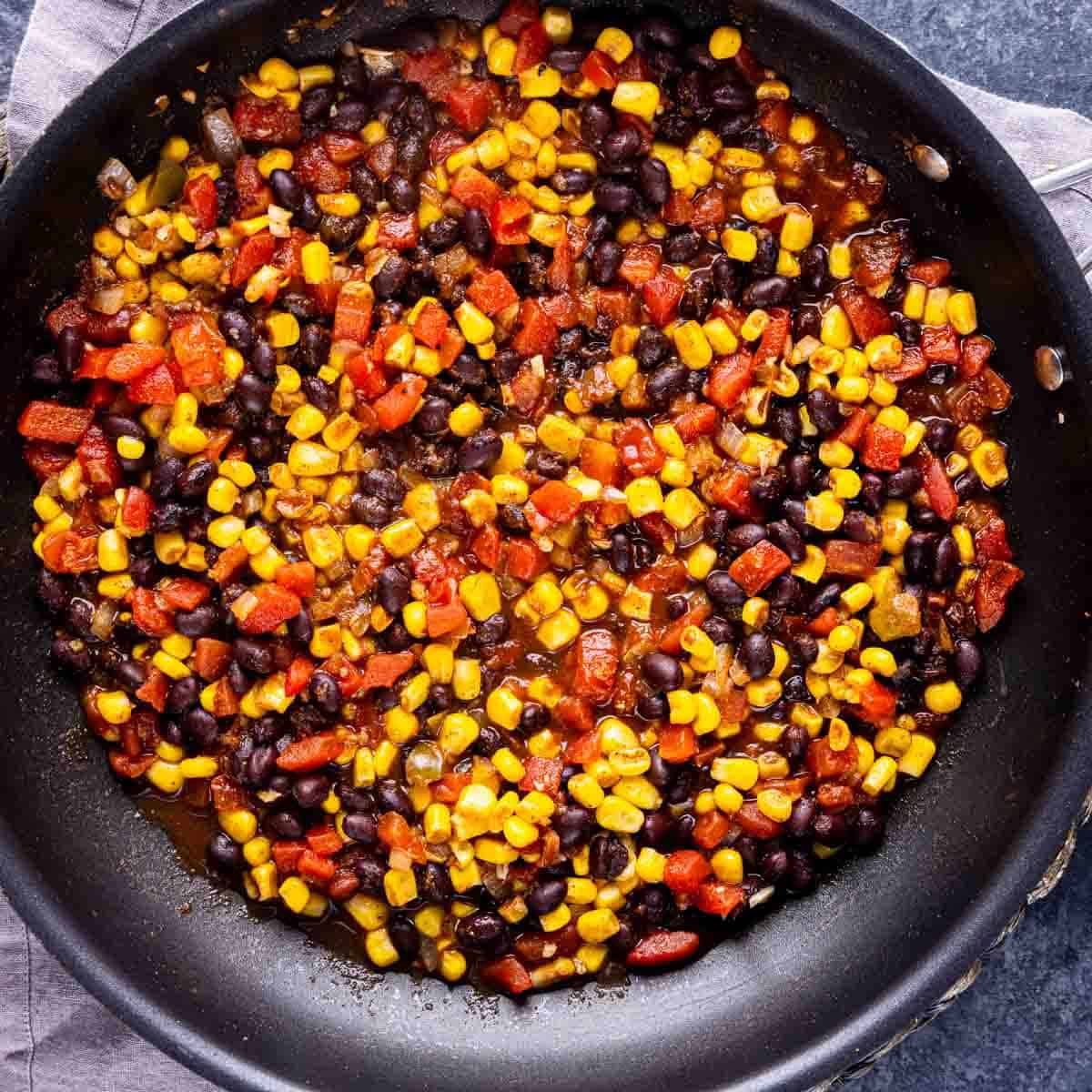 A skillet with One Pot Mexican Chicken and Rice, mixed sautéed vegetables including corn, black beans, and red peppers.